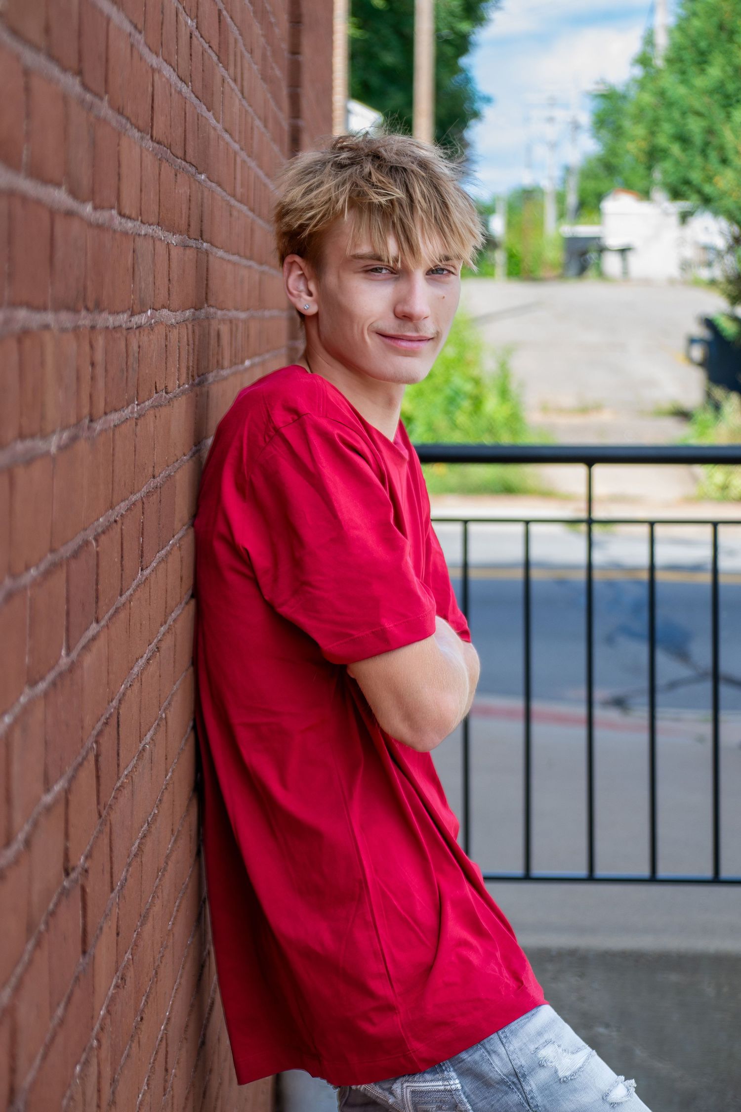 Young person in blue henley shirt sitting casually outdoors with a bright smile.