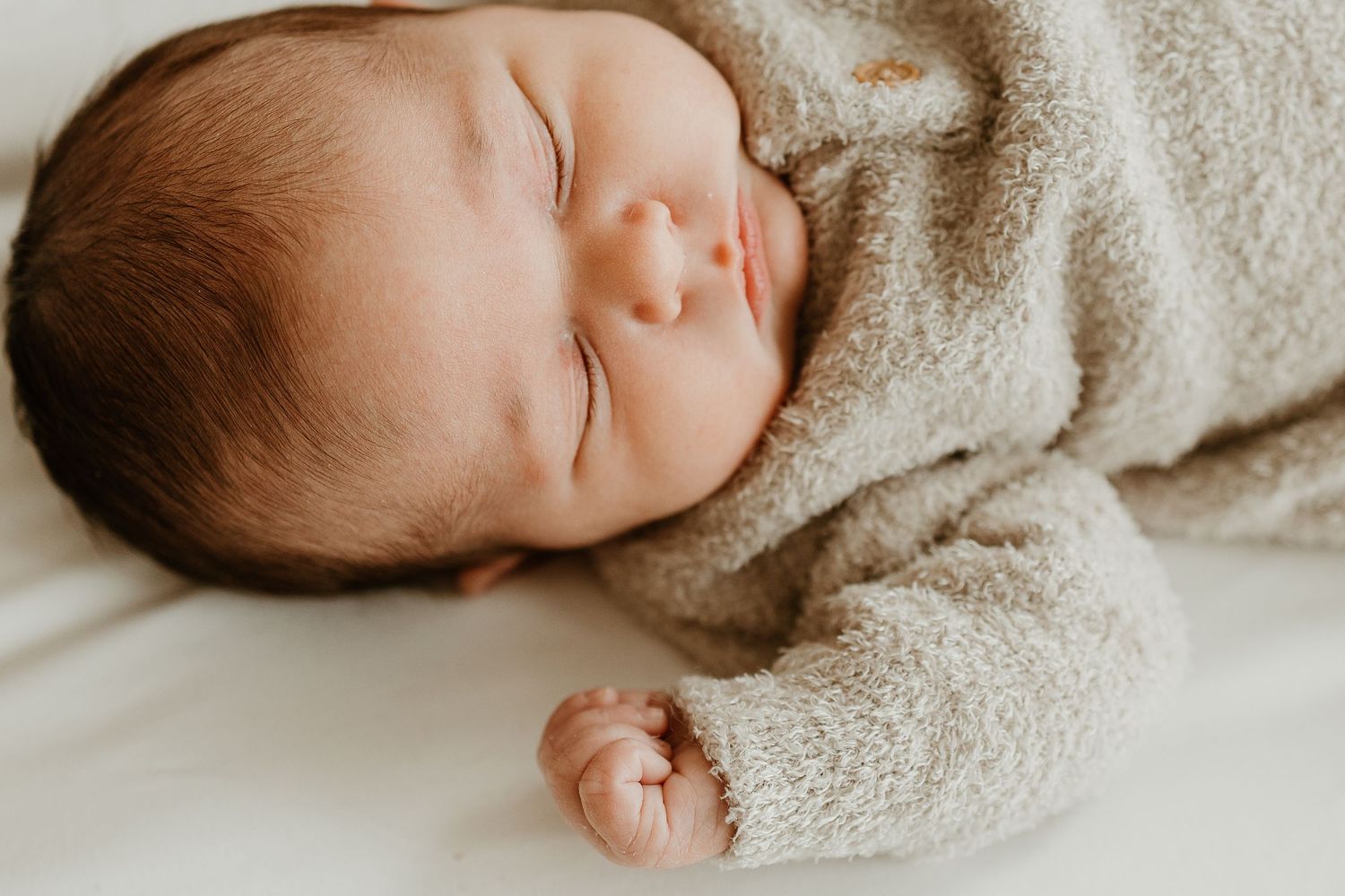 Sleeping newborn wrapped in soft beige blanket during professional photo session.