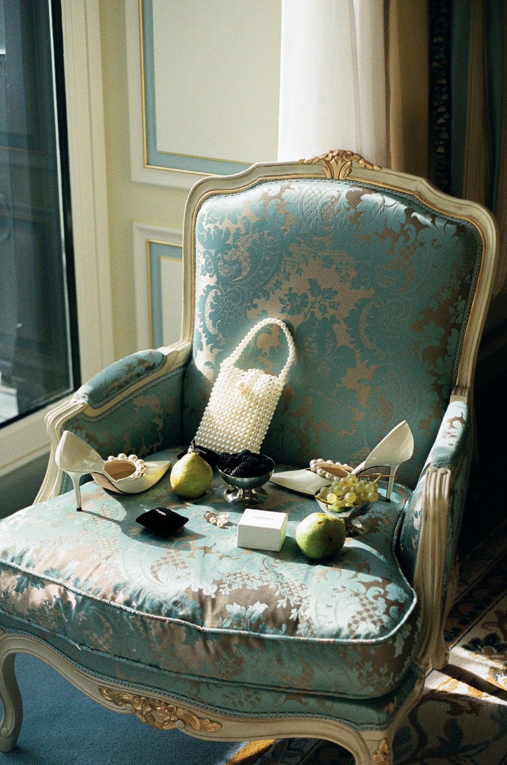 Vintage French-style armchair upholstered in faded turquoise damask fabric with ornate carved wood frame and decorative pillows.