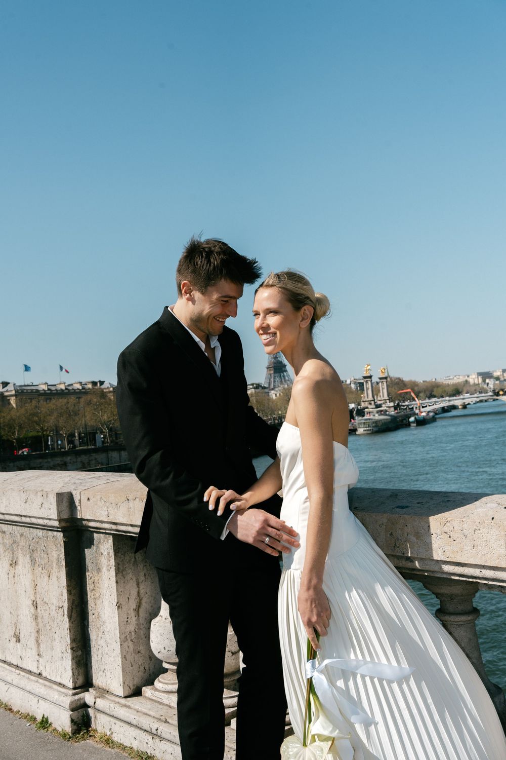 A couple in formal wedding attire share an intimate moment along Seine. Editorial fashion wedding Paris. Paris film photography.
