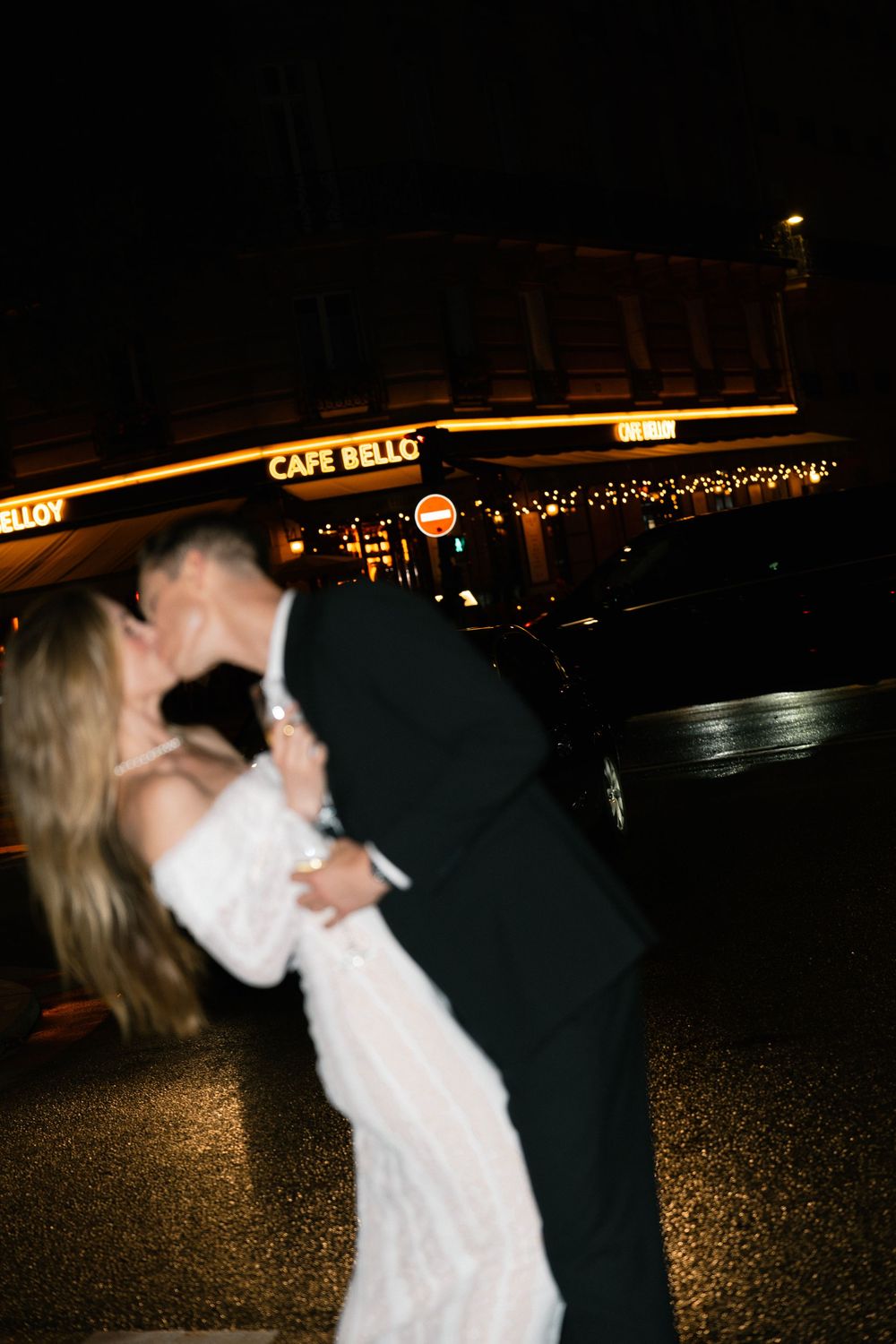 A couple in formal attire dances together at night with illuminated buildings visible in the background.