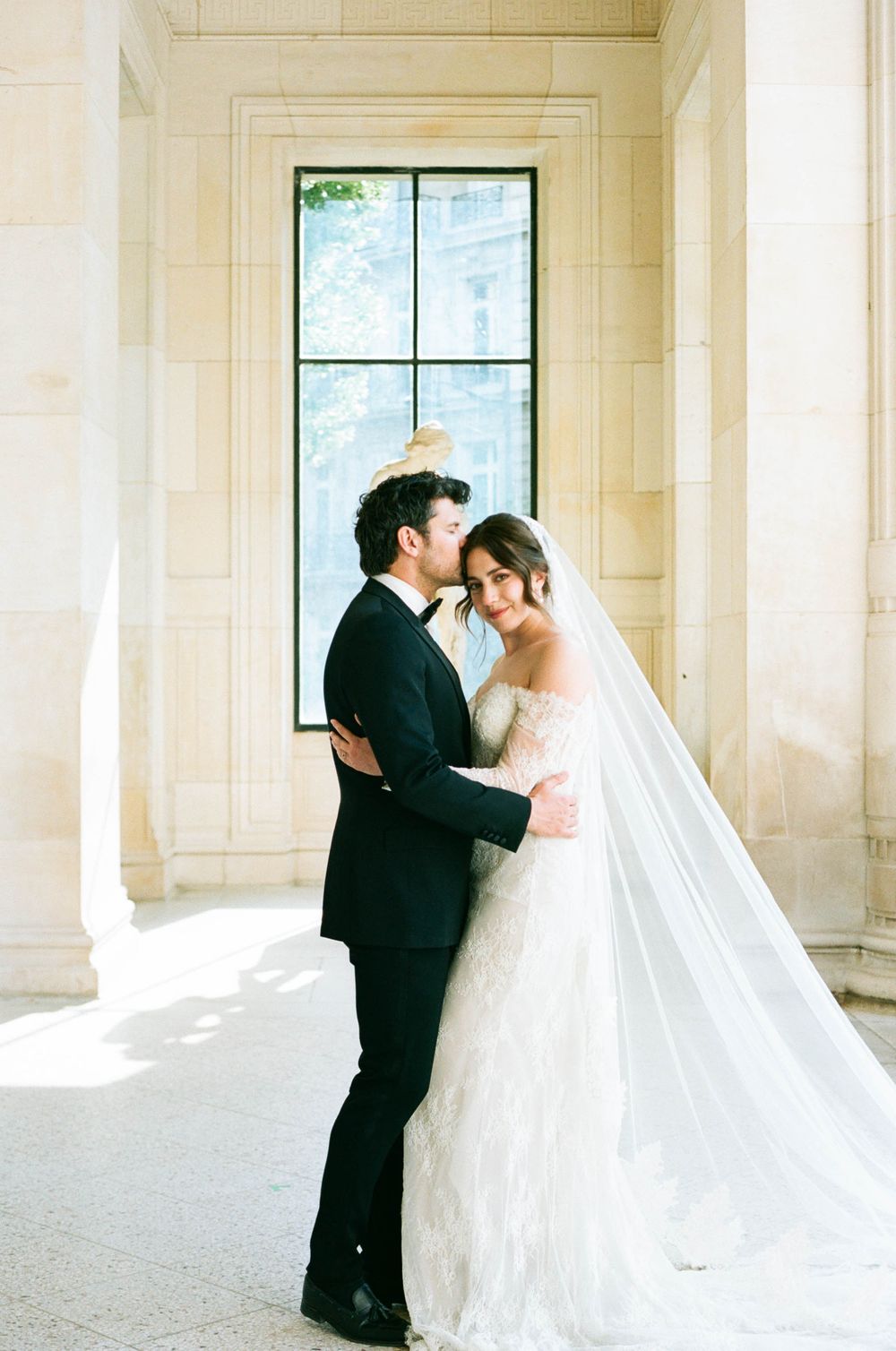 Newlywed couple shares intimate moments in an elegant gallery with white stone columns and natural light.