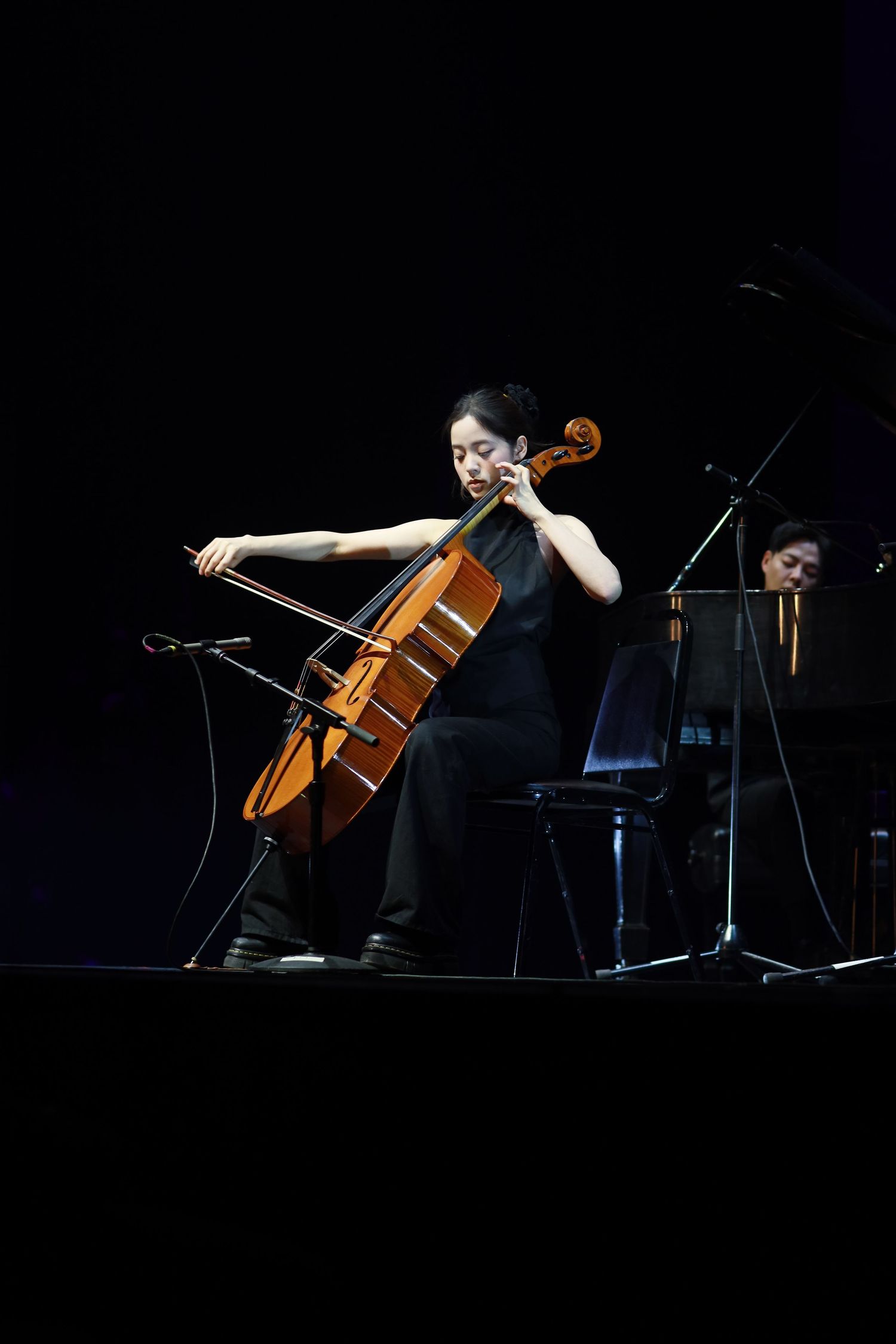 Classical musician performs on cello on dark stage during concert performance.