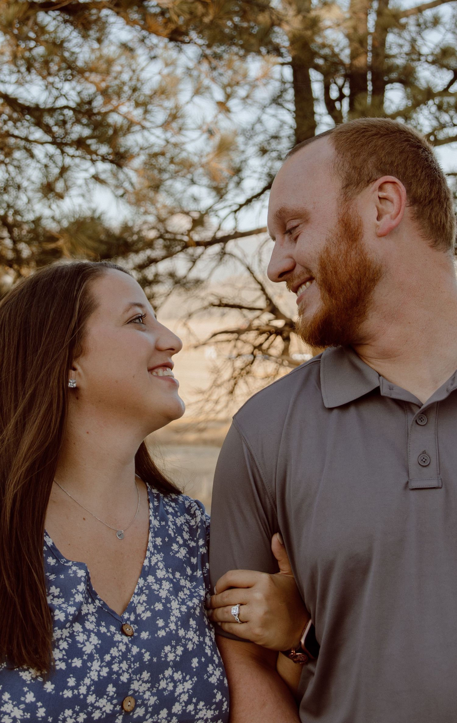 A couple shares a tender moment outdoors during golden hour, smiling and looking at each other lovingly.