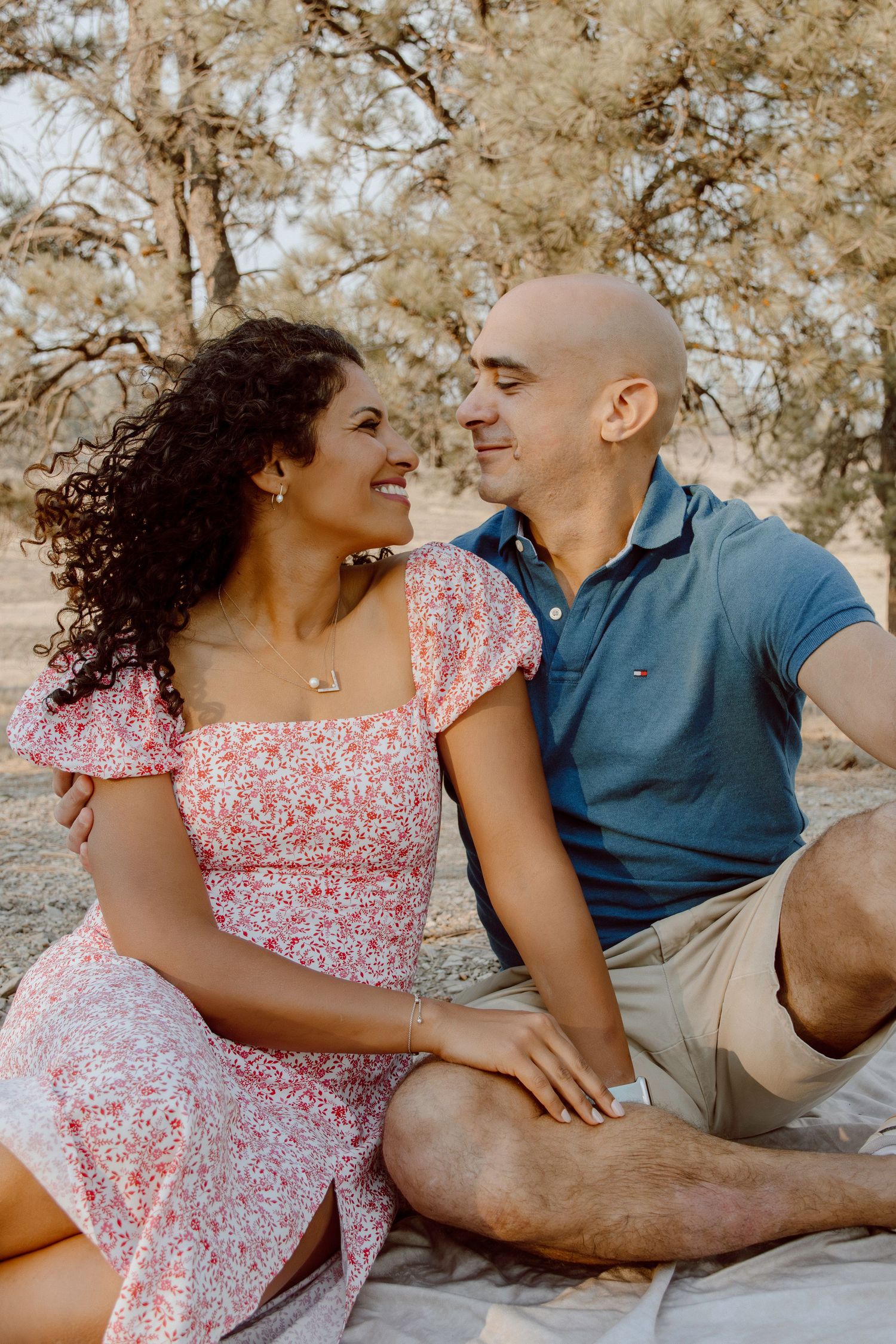 Couple sitting on blanket outdoors sharing intimate moment in warm sunlight with trees in background.