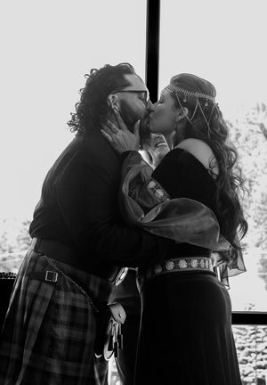 A romantic black and white photo of a couple in medieval Renaissance attire sharing a kiss at an outdoor festival.