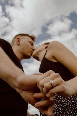 Sequence of couples holding hands against a cloudy sky background, with an engagement ring visible in the final frame.
