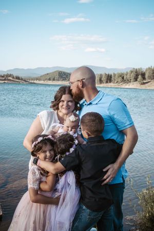 A loving family embraces together beside a scenic mountain lake on a sunny day.