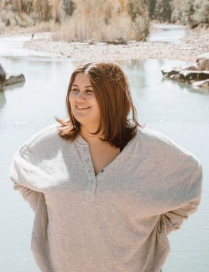 A cozy portrait in a beige sweater against a serene waterfront backdrop.