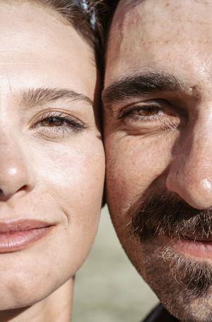 Close-up view of a smiling couple with facial features in focus against a light background.