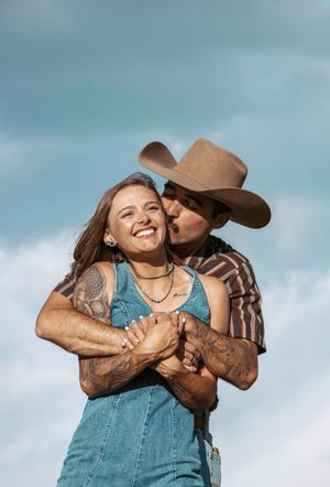 Candid series of romantic couple embracing and laughing against cloudy sky in rustic western attire.
