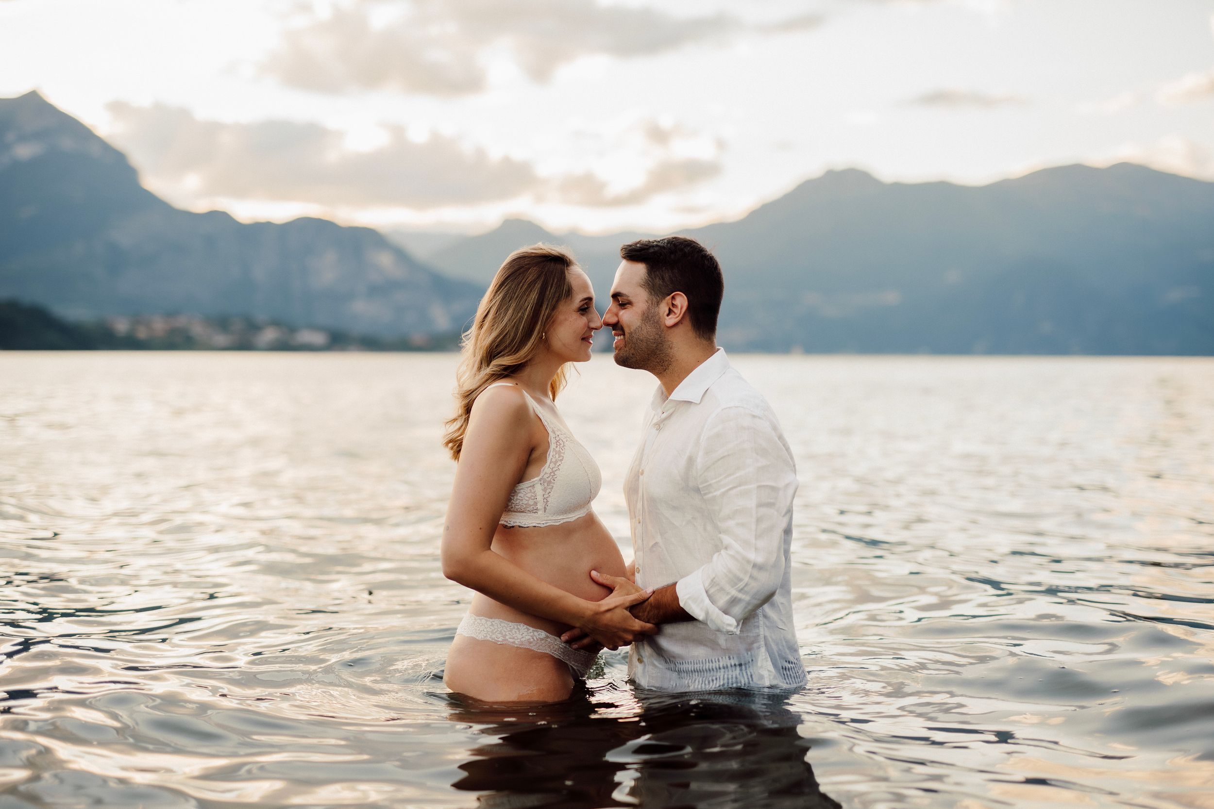 Coppia di futuri genitori nelle acque del Lago di Como accarezzano il pancione della mamma e sorridono sfiorandosi il naso