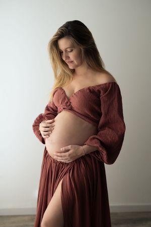 Giovane ragazza incinta in posa per un servizio fotografico accarezza delicatamente il pancione messo in evidenza da un abito in due pezzi