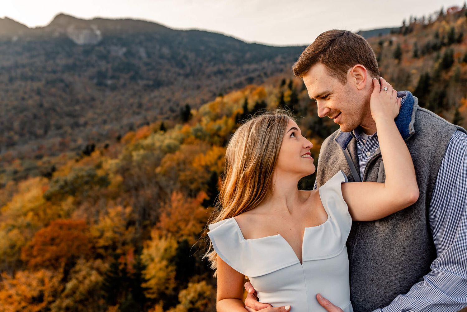Happy couple embracing with colorful autumn mountain foliage backdrop during golden hour engagement shoot.