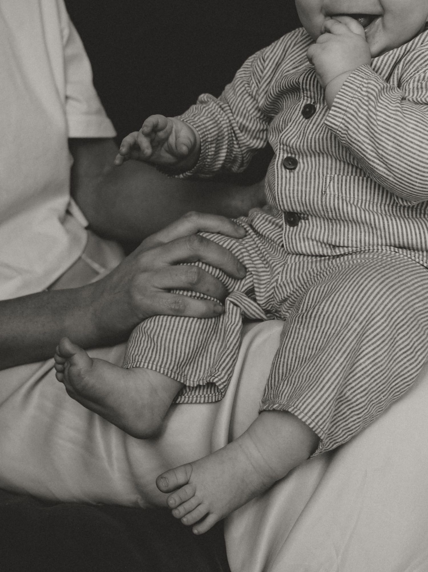 Close-up black and white photo showing gentle hands holding tiny baby feet in striped clothing.