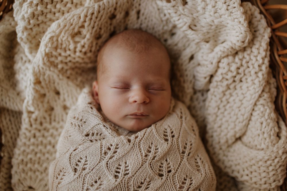 A peaceful sleeping newborn wrapped in detailed knit blankets with creamy white textures.