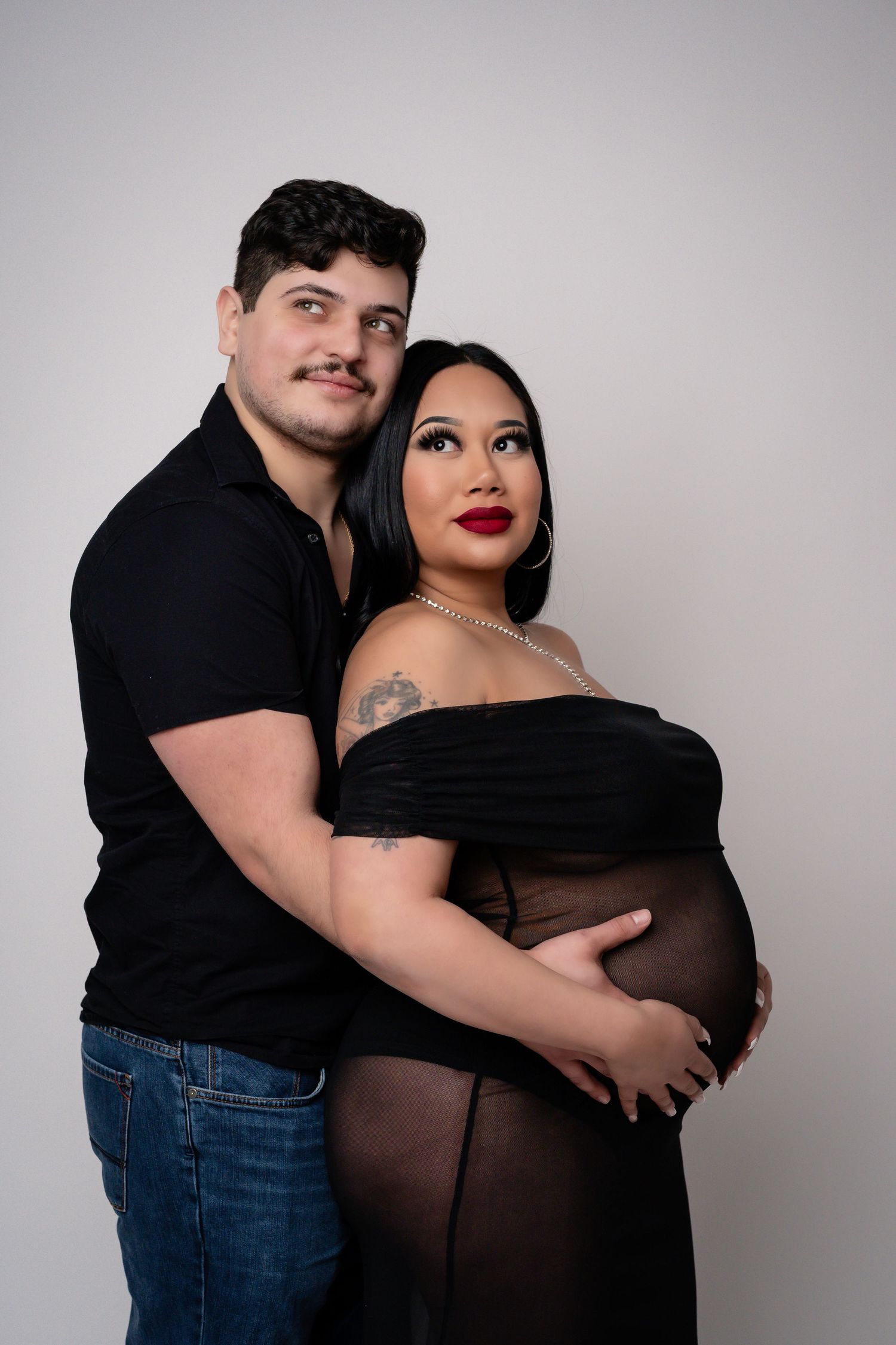 Studio portraits showcase tender moments between expectant parents in casual black and denim attire.