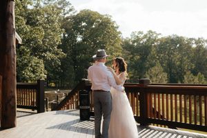 Bride and groom share a romantic moment on a wooden deck surrounded by lush green trees on their wedding day.