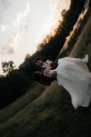 Bride and groom spinning in a field at sunset, wedding dress flowing dramatically in motion.