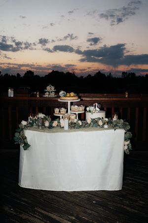Elegant wedding cake table with floral decor against a stunning sunset sky.