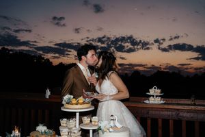 Bride and groom sharing a kiss at sunset beside a wedding dessert table with cupcakes and cake.