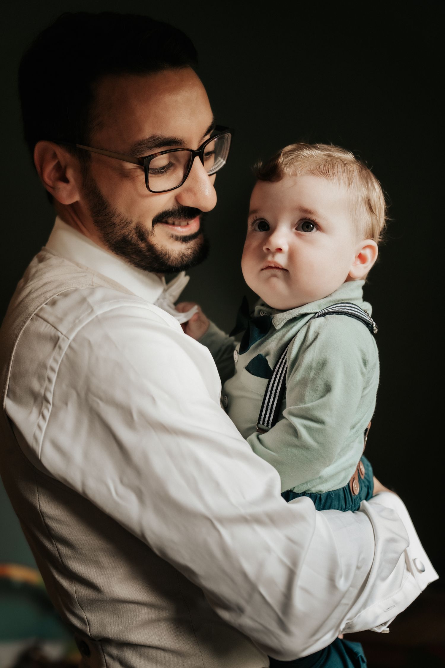 Tender moment between parent and child in formal attire against dark background.
