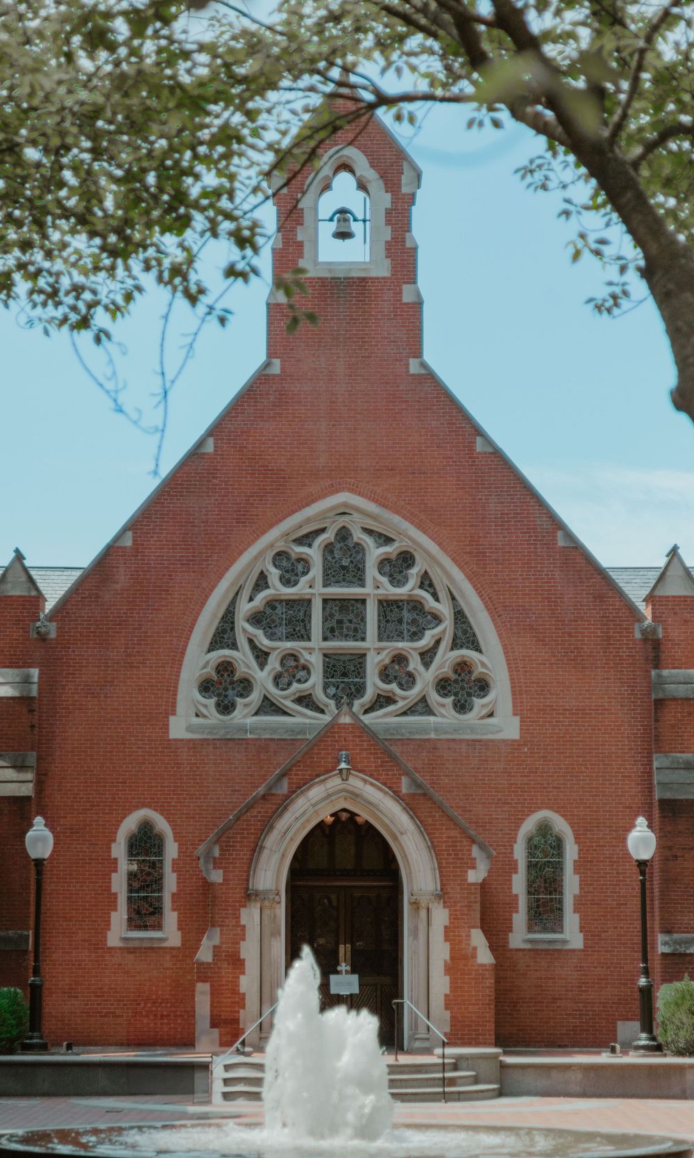 Historic red brick church with Gothic architecture and fountain in foreground.
