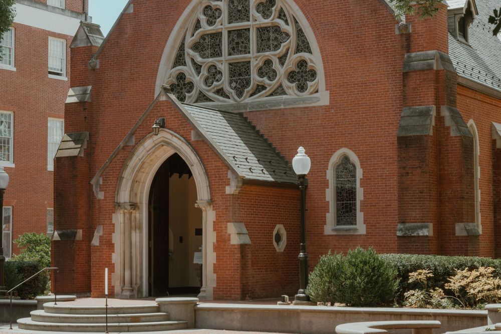 Exterior of a red brick church with Gothic arched doorway and ornate stone details.