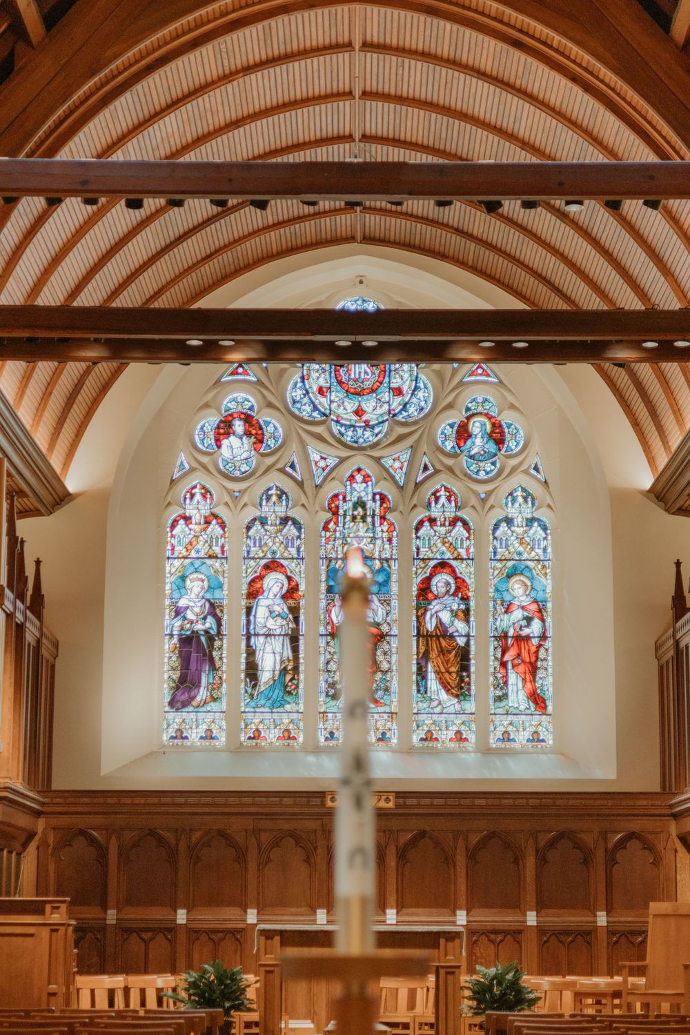Beautiful stained glass window with religious figures under vaulted wooden ceiling in church sanctuary.
