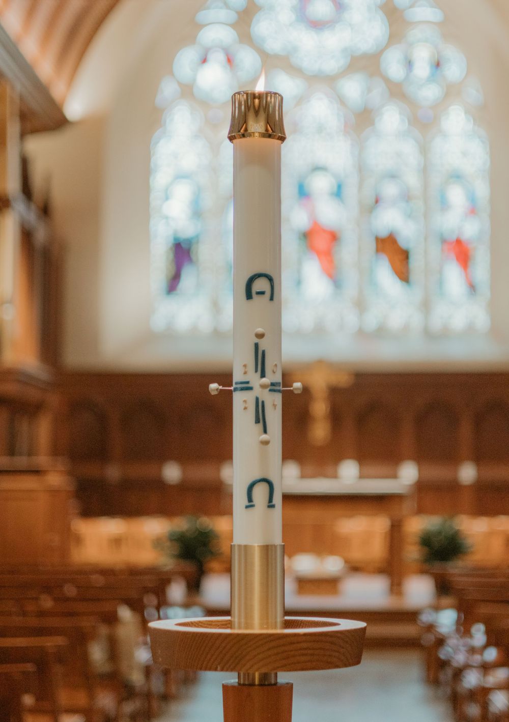Ceremonial candle with cross symbol in front of colorful stained glass church windows.