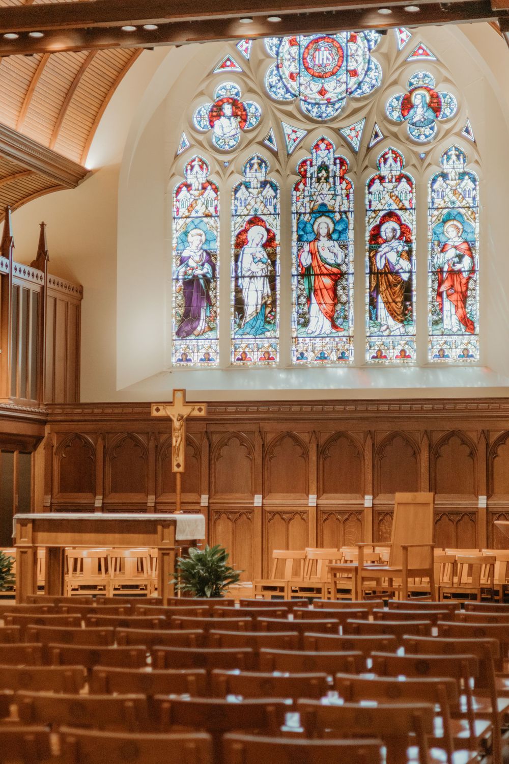 Church sanctuary with wooden pews and large stained glass window depicting religious figures.