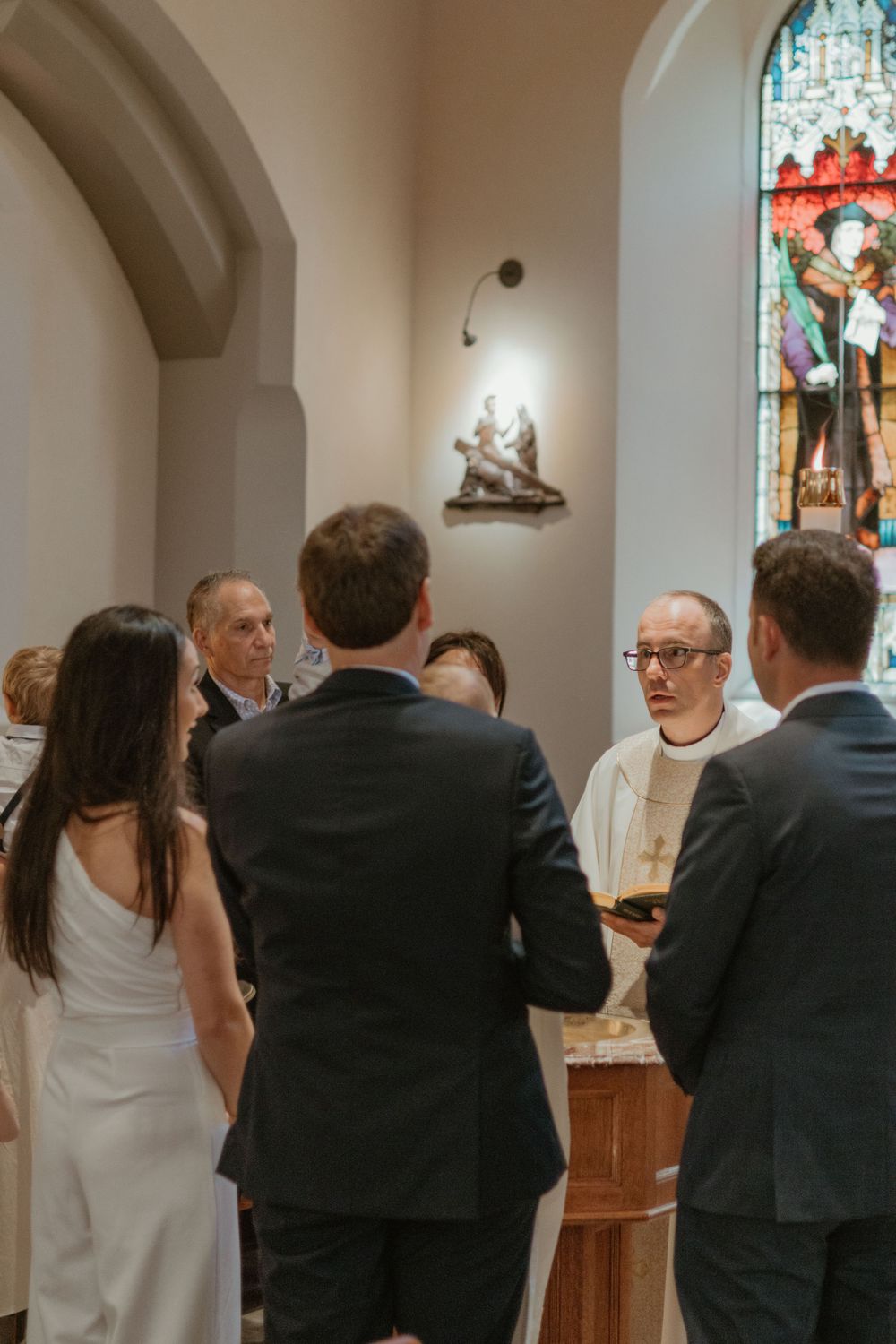 Religious ceremony taking place in church sanctuary with stained glass windows.