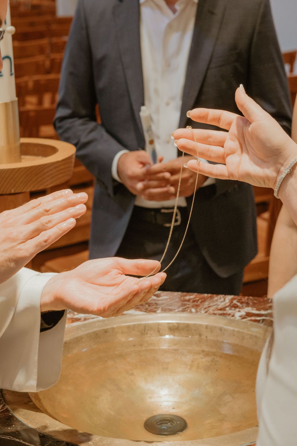 Hands exchanging necklace over a golden baptismal font during religious ceremony.