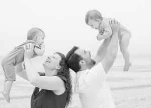 Playful family portrait in black and white — kids giggling as parents hold them high