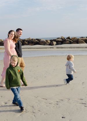 Candid beach session — parents and kids strolling near rocks morning sky
