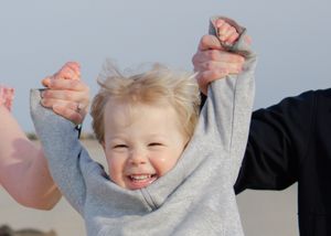 Carefree childhood moment, child with raised arms soaring above parent’s hands.