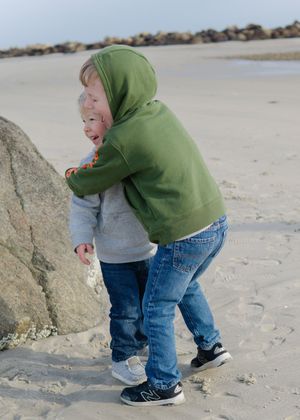Playful sibling moment, children enjoying sandy beach and exploring rocks.