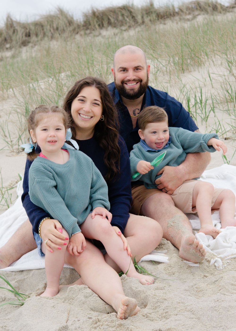 Relaxed family photo, parents and kids enjoying quiet moment together in coastal dunes.