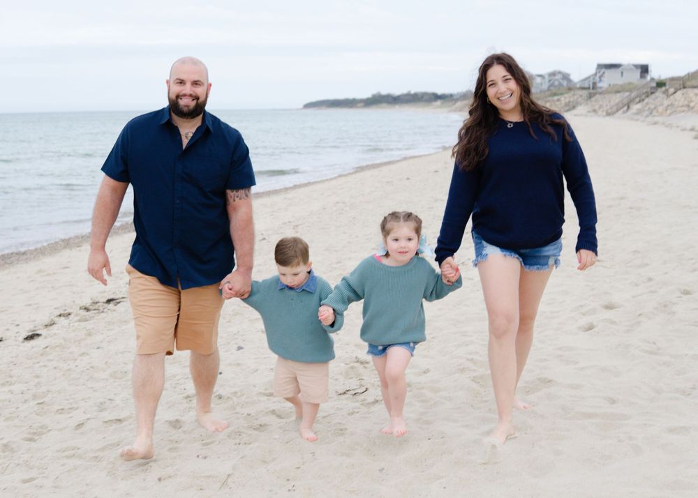Joyful Cape Cod beach portrait, family walking barefoot on sandy shore under gray sky.