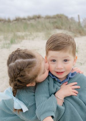 Two children in matching sweaters sharing a sweet hug on a sandy Cape Cod beach.