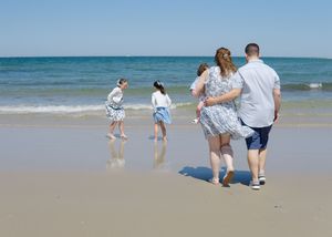 Candid beach session, sisters laughing in the waves as parents cradle baby nearby.