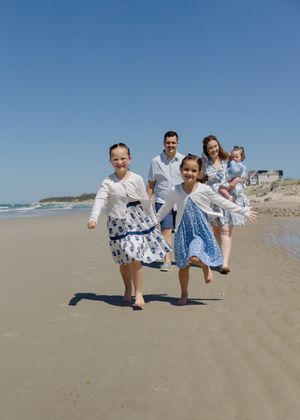 Playful family moment, matching blue and white clothing, running hand-in-hand on sandy beach