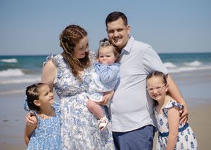 Coastal family photo session, group dressed in blue and white, standing on sandy beach.