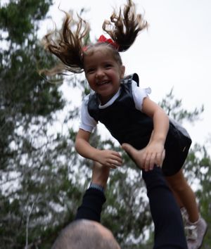 Joyful outdoor portrait, pigtail-haired child captured midair with happy expression.
