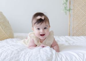 Soft, natural portrait, baby in delicate lace dress smiling on white bedding.