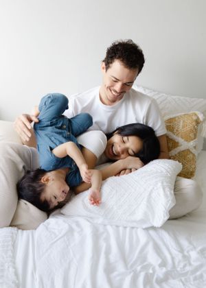 Candid lifestyle session, family laughing and cuddling on bed in natural light.