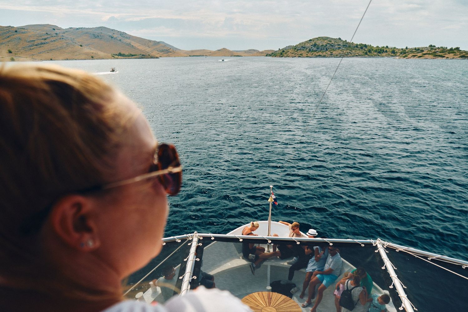 View from the bow of a boat sailing through blue waters with distant islands.