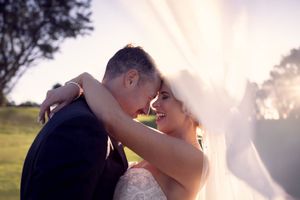 Bride and Groom under vail with golden soft sunlight behind illuminating the vail and faces