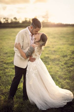 Beautiful bride is kissed by the groom at sunset surrounded by a golden glow in a field