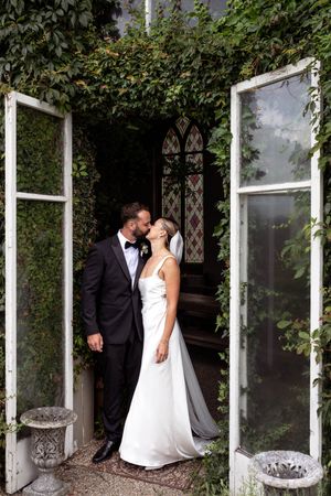 Bride and Groom embracing in a kiss surrounded by vines growing up around the wall standing in a doorway
